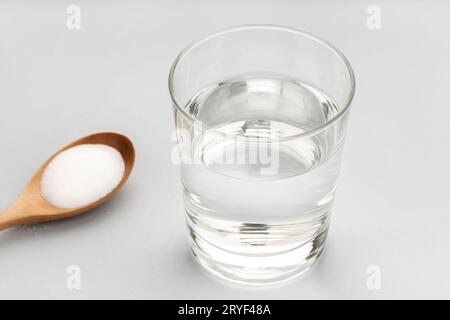 Glas Wasser und Backsoda in Holzlöffel isoliert auf grauem Hintergrund Stockfoto