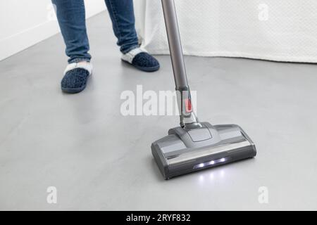 Frau, die in einem modernen Schlafzimmer mit einem kabellosen Staubsauger putzt. Speicherplatz kopieren Stockfoto