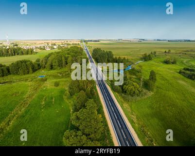 Landstraße zum Dorf zwischen Feldern vor blauem Himmel Stockfoto