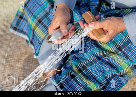 Der alte Mann strickt traditionelles Fischernetz, Hände im Rahmen Stockfoto