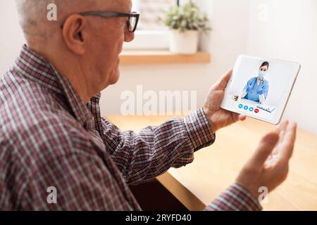 Älterer älterer Mann, der mit einer jungen Ärztin über ein Tablet-Video spricht Stockfoto