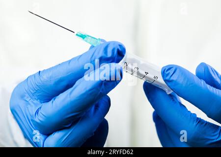 Nahaufnahme der Hände in blauen Handschuhen, die die Spritze mit Nadel halten Stockfoto