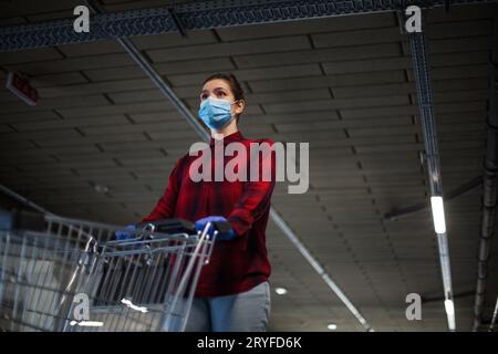 Junge Frau mit Gesichtsmaske, die einen Supermarktwagen in der Tiefgarage schiebt Stockfoto
