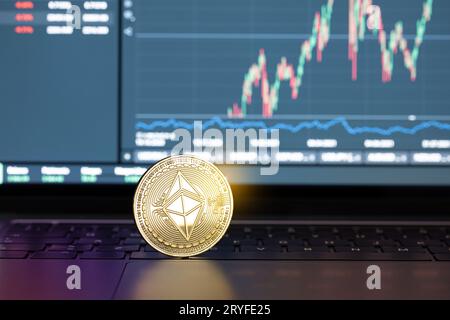 Ethereum-Münze auf Laptop und Diagramm im Hintergrund. Kryptowährungs-Handels- oder Anlagekonzept Stockfoto