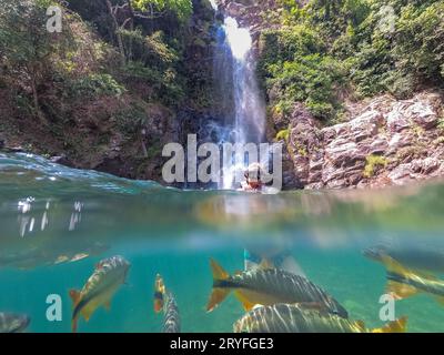 Weibliche Schnorchler und Fische unter Wasser im kristallklaren Wasserfallbecken Stockfoto