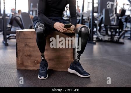 Prothetik für Menschen mit Behinderungen. Gutaussehender, brünetter Sportler mit bionischem Bein, der während der Ruhepause nach dem Workout das Smartphone benutzt, Nahaufnahme gekürzt Stockfoto