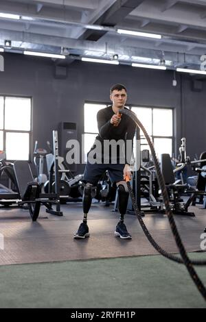 Selbstbewusster, seriöser junger Mann, der sich auf das Training mit Kampfseil, Foto in voller Länge, Hobby, Interesse, Wellness, Gesundheit und Körperpflege Stockfoto