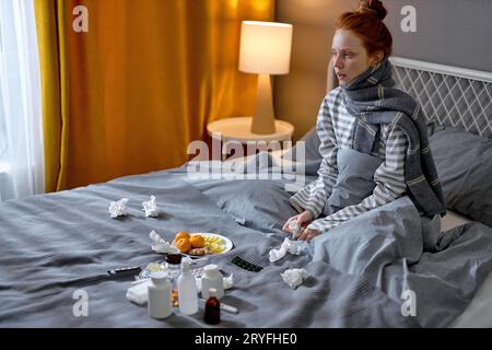 Junge, kranke, schwere, blassdepressive, rothaarige Frau mit Grippe und Erkältung, die auf dem Bett sitzt, Nahaufnahme eines Seitenbildnisses. Stockfoto