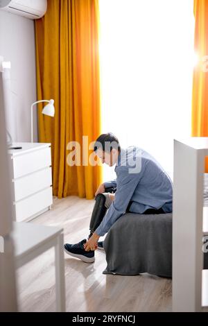 Behinderte männliche Beinamputierte mit sportlichen Sneakern auf Prothese zu Hause auf dem Bett sitzend, Behindertenschwierigkeiten nach Unfallverletzungen. Guy präpari Stockfoto
