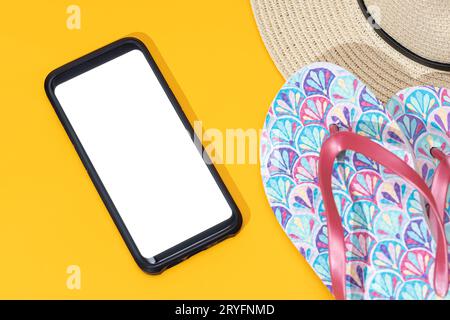 Vorlage eines Smartphones mit leerem weißen Bildschirm, Flipflops und Hut auf gelbem Hintergrund Stockfoto