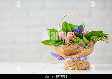 Schöner Blumenstrauß mit rosa Rosen, lila Lisianthus und grünen Blättern in einem Korb auf einem Tisch Stockfoto
