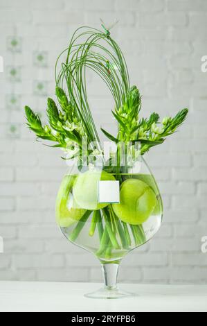 Vertikaler Schuss von Ornithogalum und Äpfeln in einem großen Glasbecher auf einem Tisch Stockfoto