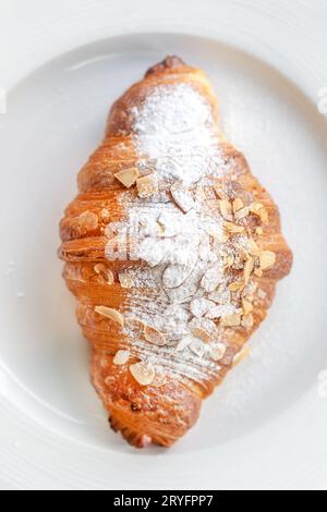 Blick von oben auf ein köstliches frisches Mandelcroissant auf einem Teller, perfekte Ergänzung zum Morgenkaffee Stockfoto