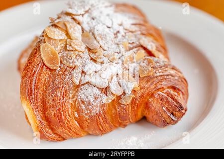 Köstliches frisches Mandelcroissant auf einem weißen Teller, perfekte Ergänzung zum Morgenkaffee Stockfoto