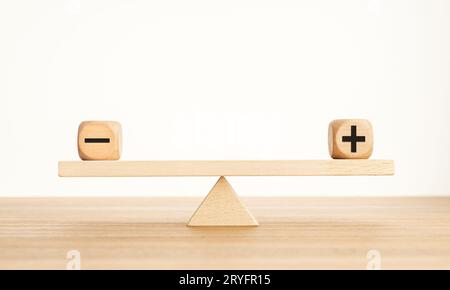 Plus- und Minus-Balance-Konzept. Positive und negative Symbole auf Holzblöcken sind auf einer hölzernen Wippe im Gleichgewicht. Speicherplatz kopieren Stockfoto