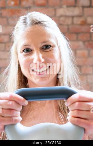 Blonde junge muskulöse Frau mit sportlichem Aussehen, die High Pull-Übungen mit Kettlebells beim harten Training im Garage-Fitnessstudio macht. Stockfoto