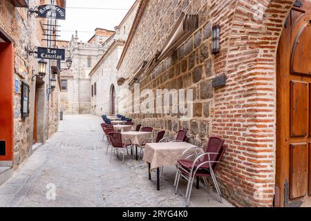 Avila, Spanien, 07.10.21. Mittelalterliche, schmale Kopfsteinpflasterstraße in Avila, Spanien, mit Restauranttischen und Essbereich, keine Leute. Stockfoto