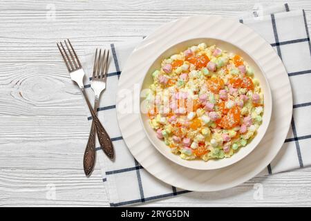 Ambrosia-Salat mit Ananas, Mandarinen, Joghurt, Mini-Marshmallows, Kokos und Schlagsahne in weißer Schüssel auf weißem Holztisch mit Gabeln, Stockfoto