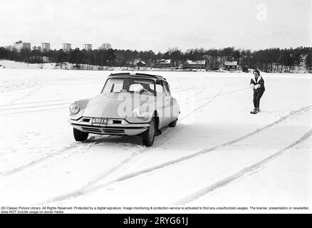 Ein Wintertag in den 1960er Jahren Eine Frau fährt hinter einem Auto. A Citroën. Es muss ziemlich dickes Eis auf dem See gewesen sein, weil der Fahrer es wagte, auf dem Eis zu fahren, aber selbst die Frau muss mutig gewesen sein, als sie sicher Geschwindigkeit auf ihren Skiern nahm, als sie an einem Seil mit einem Griff hinter dem Auto an hielt volle Geschwindigkeit. Schweden 1962. Conard Ref. 4561 Stockfoto