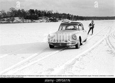 Ein Wintertag in den 1960er Jahren Eine Frau fährt hinter einem Auto. A Citroën. Es muss ziemlich dickes Eis auf dem See gewesen sein, weil der Fahrer es wagte, auf dem Eis zu fahren, aber selbst die Frau muss mutig gewesen sein, als sie sicher Geschwindigkeit auf ihren Skiern nahm, als sie an einem Seil mit einem Griff hinter dem Auto an hielt volle Geschwindigkeit. Schweden 1962. Conard Ref. 4561 Stockfoto