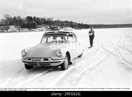 Ein Wintertag in den 1960er Jahren Eine Frau fährt hinter einem Auto. A Citroën. Es muss ziemlich dickes Eis auf dem See gewesen sein, weil der Fahrer es wagte, auf dem Eis zu fahren, aber selbst die Frau muss mutig gewesen sein, als sie sicher Geschwindigkeit auf ihren Skiern nahm, als sie an einem Seil mit einem Griff hinter dem Auto an hielt volle Geschwindigkeit. Schweden 1962. Conard Ref. 4561 Stockfoto