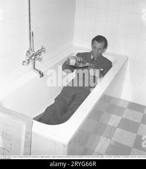 Seltsam in den 1940er Jahren Georg Rydeberg, 1907–1983, schwedischer Schauspieler. Hier liegt er in einem schönen Anzug, in einer Badewanne, wo er sich ein Glas Limonade gießt. Schweden 1945. Kristoffersson ref M87-2 Stockfoto