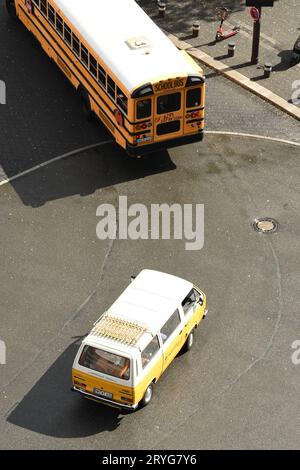 Vertikale Aufnahme eines gelb-weißen Autos, das hinter einem amerikanischen Schulbus auf einer Straße fährt Stockfoto