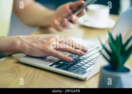 Nahaufnahme Fokus auf die Hände des Mannes, die am Computer mit Smartphone arbeiten. Technologie und Lebensstil der Menschen Menschen arbeiten Hand an Laptop und Stockfoto