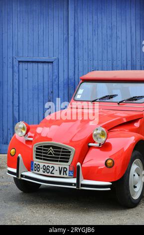 HERAULT (34). SAINT-CHINIAN. RED CITROEN CAR 2CV PARKTE VOR EINER BLAUEN TÜR EINER GARAGE IN EINER STRASSE DER VILLLAGE VON SAINT-CHINIAN. Stockfoto