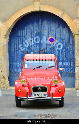 HERAULT (34). SAINT-CHINIAN. RED CITROEN CAR 2CV PARKTE VOR EINER BLAUEN TÜR EINER GARAGE IN EINER STRASSE DER VILLLAGE VON SAINT-CHINIAN. Stockfoto