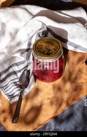 Johannisbeermarmelade in einem geschlossenen einmauerglas auf einem Schneidebrett, mit einem Küchentuch und einem Löffel Stockfoto