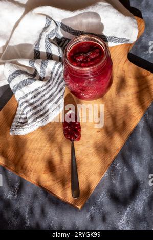 Johannisbeermarmelade in einem einmachglas auf einem Schneidebrett, mit einem Geschirrtuch, Marmelade in einem Löffel Stockfoto