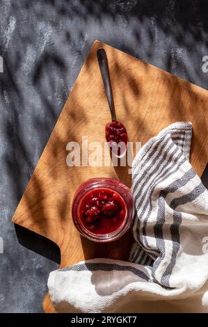 Johannisbeermarmelade im mauerglas auf dem Schneidebrett, mit Küchentuch, Marmelade im Löffel, Blick von oben Stockfoto