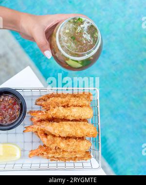 Panierte Garnelen mit Chili-Sauce, Zitronenscheibe und Cocktail in der Hand, serviert am Swimmingpool Stockfoto