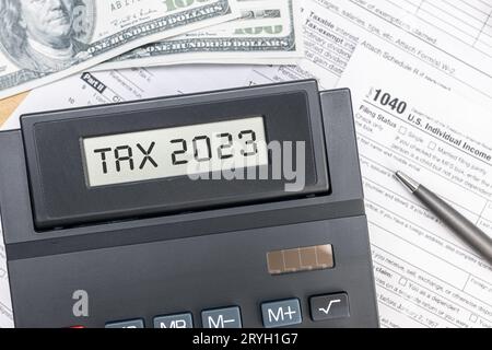 Tax Time 2023-Konzept. Text auf dem Bildschirm des Rechners, Tex-Formulare und Dollarscheine auf dem Tisch. Draufsicht Stockfoto