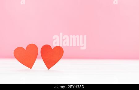 Hintergrund zum Valentinstag. Zwei rote Holzherzen auf einem weißen Tisch auf pinkfarbenem Hintergrund. Speicherplatz kopieren Stockfoto
