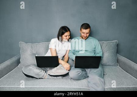 Ein junges lächelndes Paar, das sich auf dem Sofa mit ihren Laptops entspannt Stockfoto