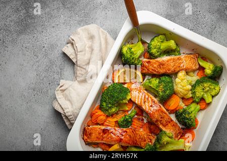 Blick von oben auf gesunde gebackene Fisch Lachssteaks, Brokkoli, Blumenkohl, Karotte in Auflaufform auf grauem Steinhintergrund. Kochen Stockfoto