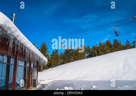 Eine Gruppe von Skifahrern, die mit dem Sessellift fahren. Gebäude mit Eiszapfen, die vom Dach hängen, Andorra Stockfoto