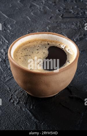 Kaffeetasse. Espresso mit Schaum in einem einfachen braunen Becher auf schwarzem Hintergrund Stockfoto