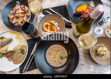 Auswahl an Meeresfrüchten und mediterranen Gerichten. Traubenschnecken, Wolfsbarschfilet, gebackene Austern, Pilzsuppe. Hochwertige Fotos Stockfoto