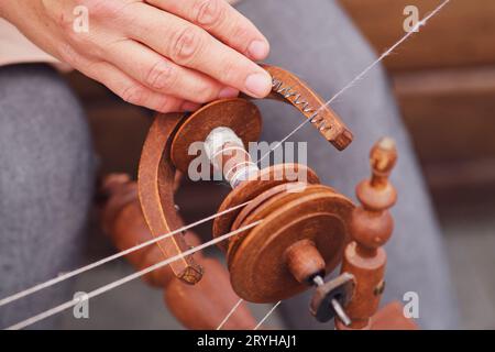 Die Nahaufnahme zeigt einen sich von Hand drehenden Faden auf einem alten Drehrad. Nahaufnahme der Hände einer Frau, die Faden auf einem drehenden Rad weben Stockfoto
