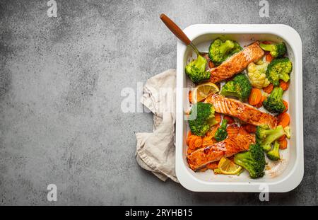 Blick von oben auf gesunde gebackene Fisch Lachssteaks, Brokkoli, Blumenkohl, Karotte in Auflaufform auf grauem Steinhintergrund. Kochen Stockfoto