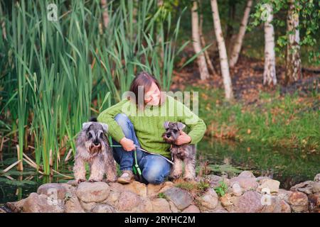 Reife Frau, die auf einem Stein sitzt, mit zwei Miniatur-Schnauzer-Hunden Stockfoto