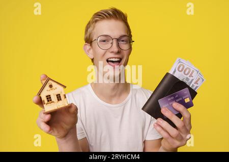 Finanzierungskonzept Für Hauskauf. Ein glücklicher junger Mann hält in den Händen eine Geldbörse mit Geld und eine Kreditkarte, um sein Haus zu kaufen. Stockfoto