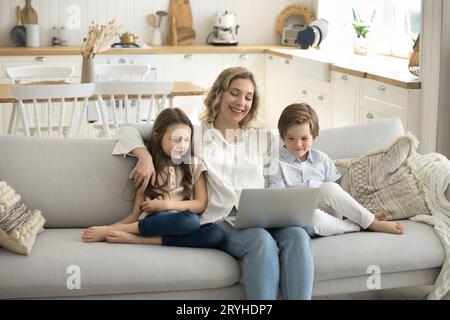 Sorglose Mutter mit zwei Kindern schaut sich lustige Videos auf dem Notebook an Stockfoto