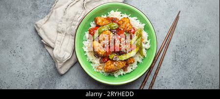 Asiatisches süß-saures Hähnchen mit Gemüse, gebraten und Reis in einer Keramikschale mit Stäbchen von oben, grauer rustikaler ston Stockfoto