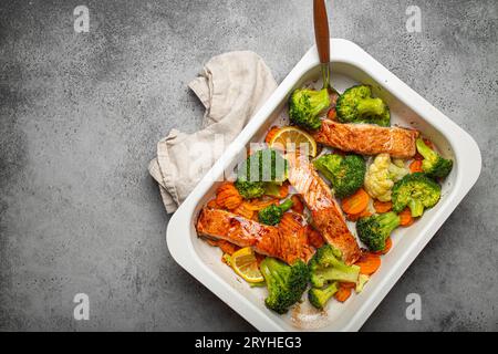 Blick von oben auf gesunde gebackene Fisch Lachssteaks, Brokkoli, Blumenkohl, Karotte in Auflaufform auf grauem Steinhintergrund. Kochen Stockfoto