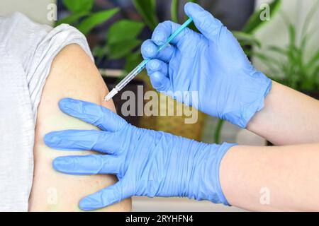 Nahaufnahme der Hände in blauen Handschuhen bei einer Impfung in der Schulter des Patienten. Grippeimpfung, Injektion am Arm. Coronavirus-covid-19-Impfstoff. Cov Stockfoto