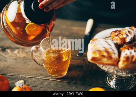 Weibliche Hand hält eine Teekanne aus Glas und gießt heißen aromatischen Tee in die Tasse Stockfoto